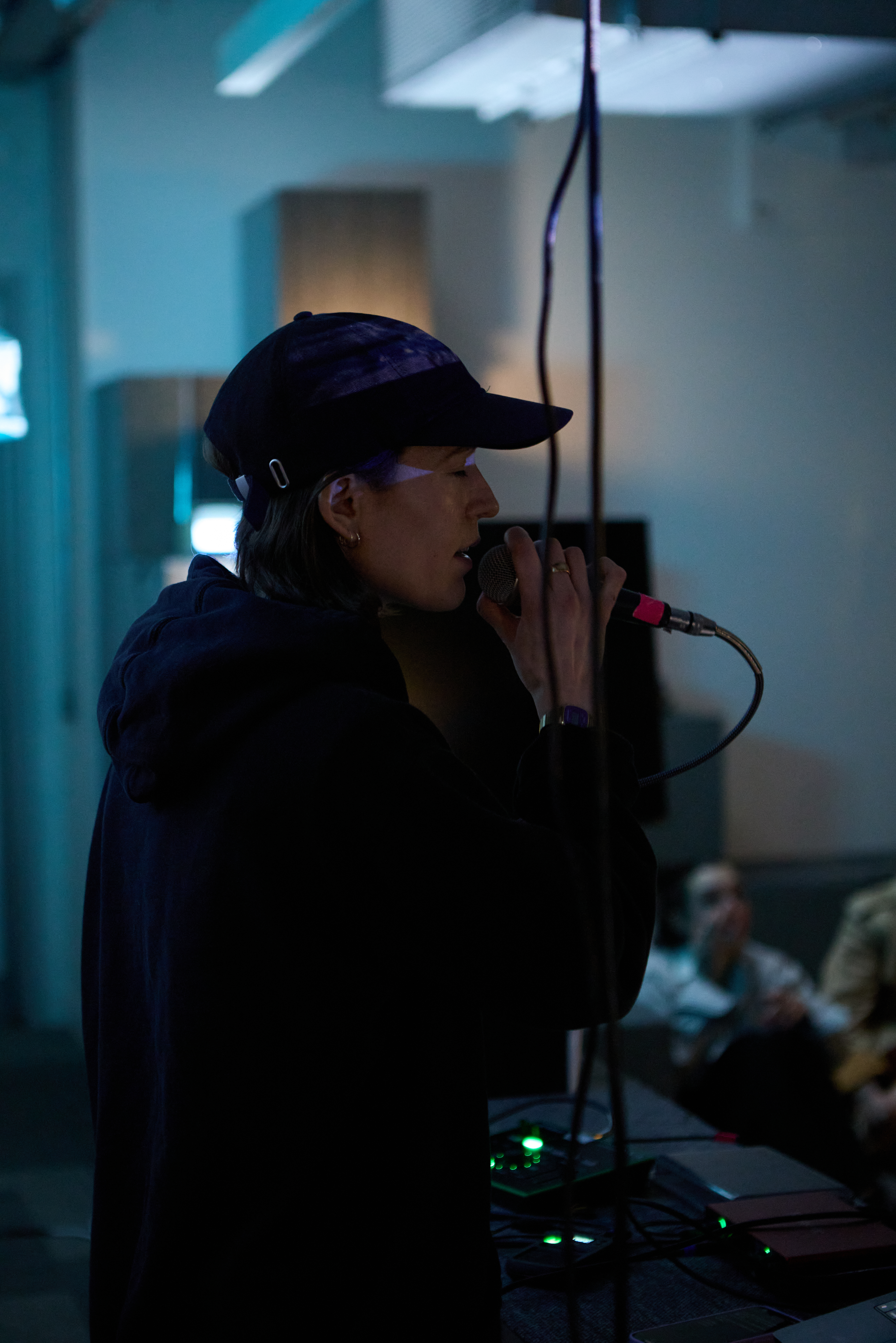 Side profile of I. Nakhla performing, they are speaking/singing into a microphone.