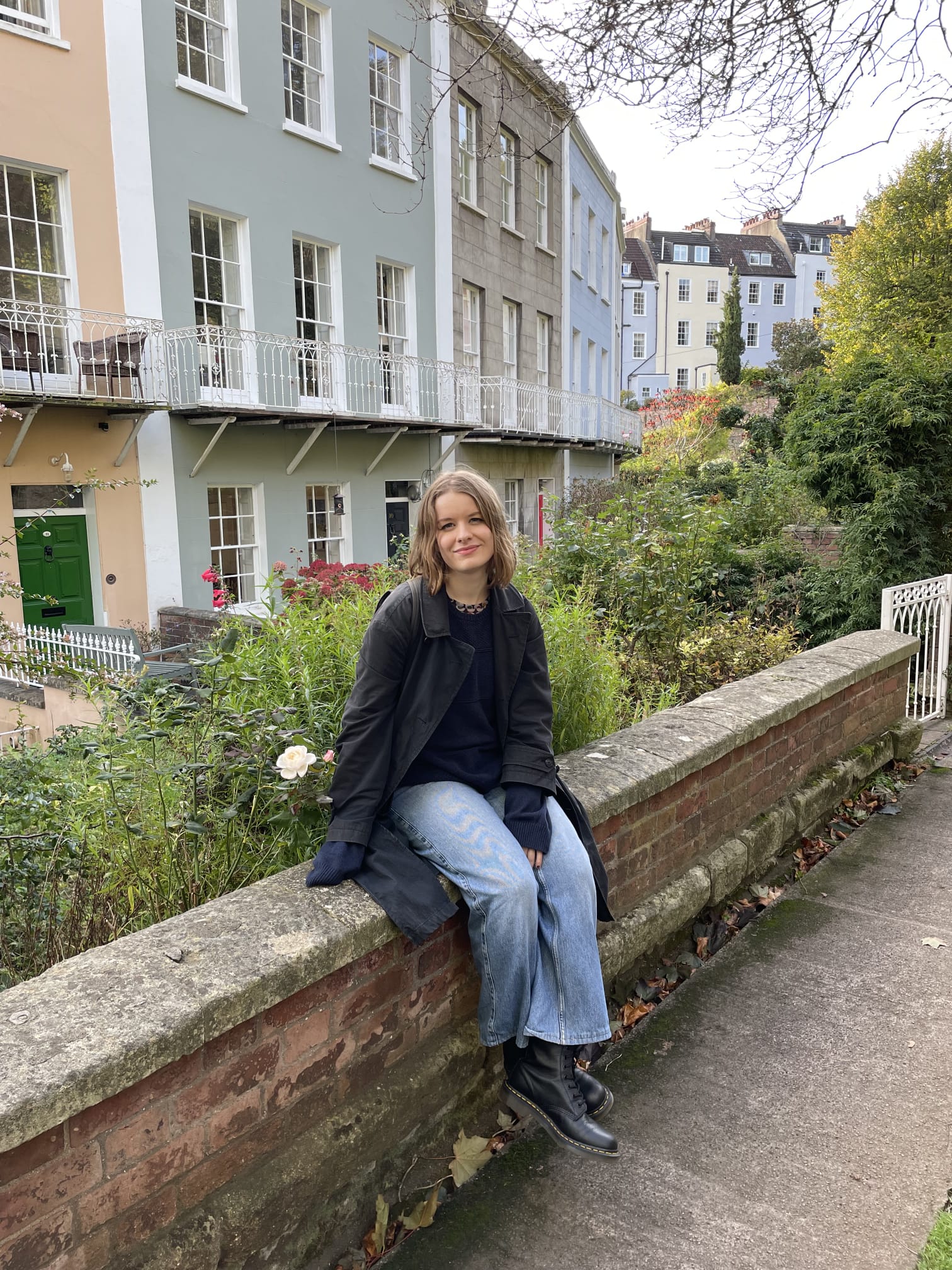 Photo of Mia sitting on a wall, facing the camera and smiling.