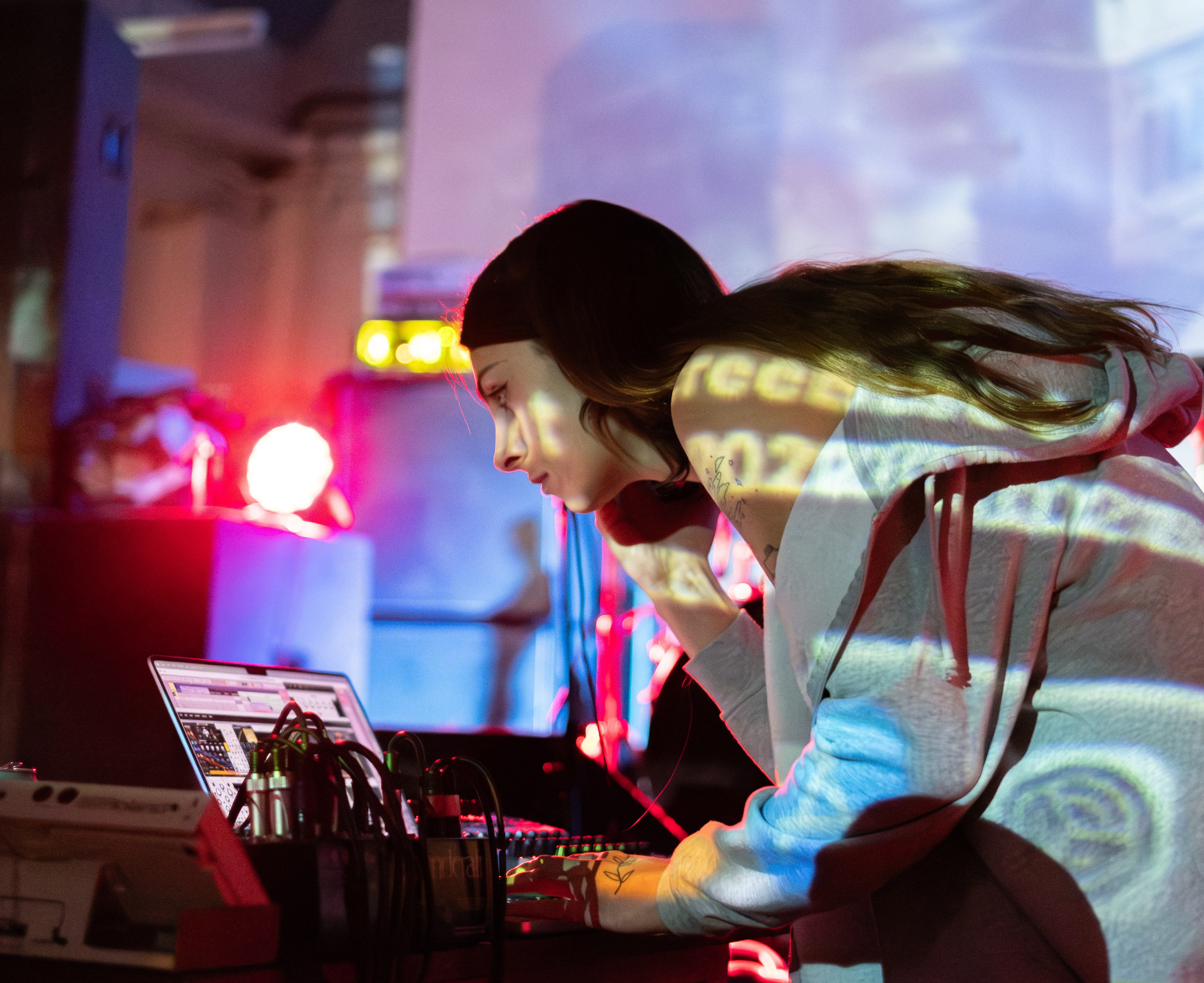 Photo of Theia performing with a laptop. A projection of the mac system preferences can be seen across her arm.